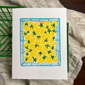 Puede incluir: Una ilustraci&oacute;n dibujada a mano de una caja llena de tomates amarillos. Los tomates est&aacute;n dibujados en un estilo simple y de dibujos animados con tallos verdes. La caja est&aacute; delineada en azul.