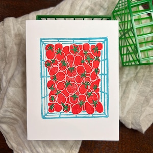 Puede incluir: Una impresi&oacute;n de lin&oacute;leo de una cesta azul llena de tomates rojos. Los tomates est&aacute;n dispuestos en un patr&oacute;n aleatorio y tienen tallos verdes.
