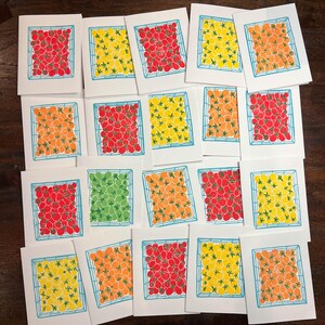 Puede incluir: Una colecci&oacute;n de 18 tarjetas con una cuadr&iacute;cula de tomates en varios colores, incluyendo rojo, naranja, amarillo y verde. Las tarjetas est&aacute;n dispuestas en una cuadr&iacute;cula sobre una superficie de madera.