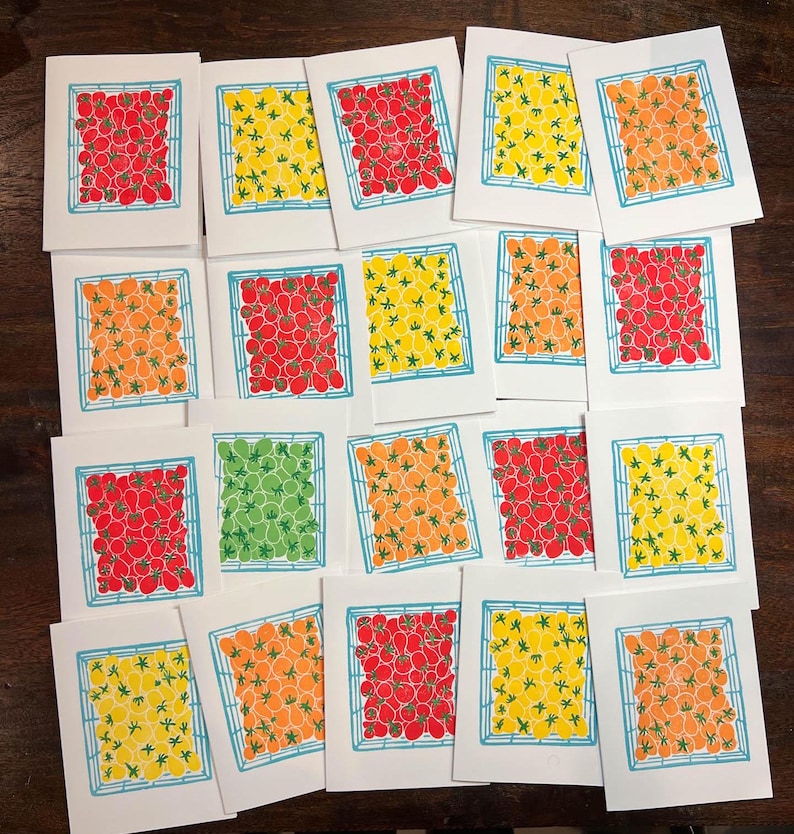 Puede incluir: Una colecci&oacute;n de 18 tarjetas con una cuadr&iacute;cula de tomates en varios colores, incluyendo rojo, naranja, amarillo y verde. Las tarjetas est&aacute;n dispuestas en una cuadr&iacute;cula sobre una superficie de madera.