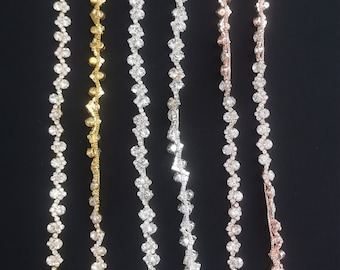 May include: Four strands of rhinestone chain trim, each with a different metal finish: gold, silver, rose gold, and silver. The chains are made of small, round rhinestones connected by metal links.