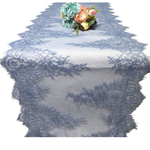 Könnte beinhalten: Ein hellblauer Tischläufer aus Spitze mit einem gewellten Rand. Der Läufer ist mit einem zarten Blumenmuster verziert. Ein Strauß aus rosa und weißen Blumen liegt auf dem Läufer.