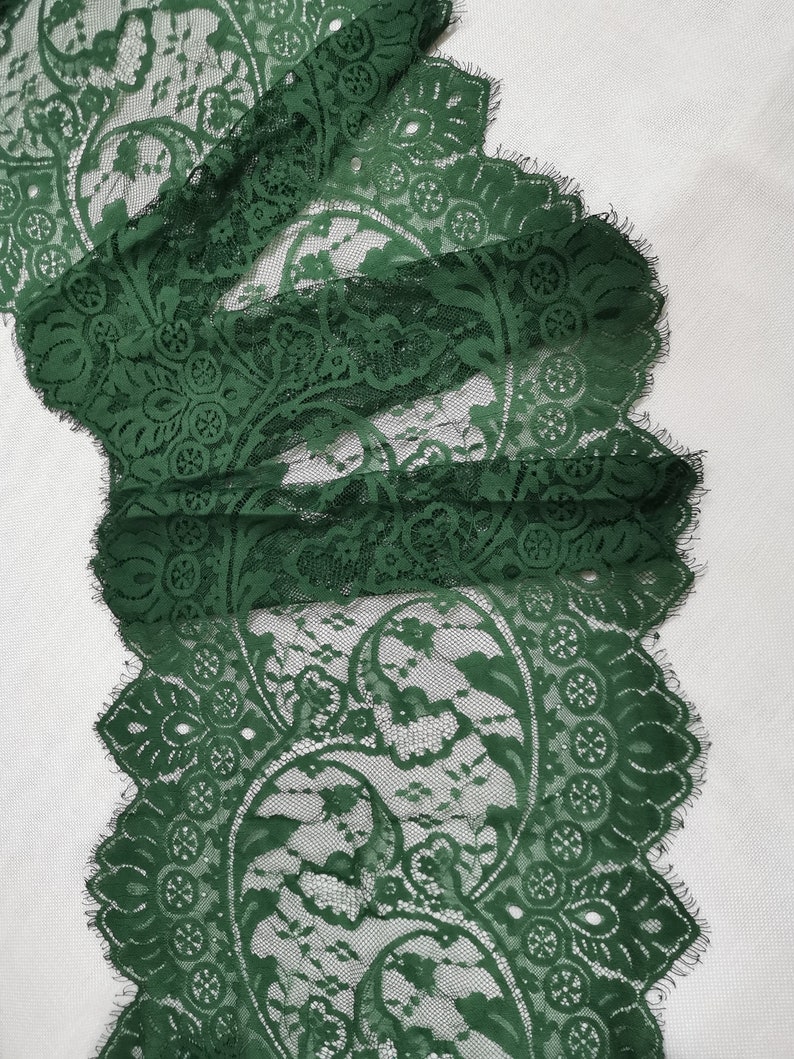 May include: Green lace trim featuring a paisley pattern. The lace has a scalloped edge and a delicate, intricate design.