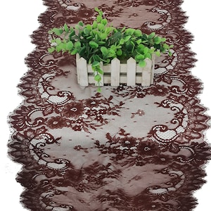 May include: Brown lace table runner with a scalloped edge. The runner is made of delicate lace with a floral pattern.