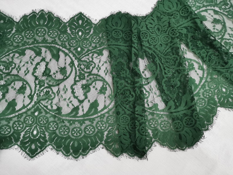 May include: Green lace trim with a delicate floral pattern. The lace has a scalloped edge and a frayed finish.