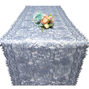 May include: A blue lace table runner with a delicate floral pattern. The runner is made of a soft, lightweight fabric and has a scalloped edge.