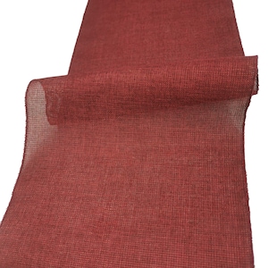 Puede incluir: Un rollo de cinta de arpillera roja. La cinta está tejida con un patrón texturizado y tiene una superficie ligeramente rugosa.