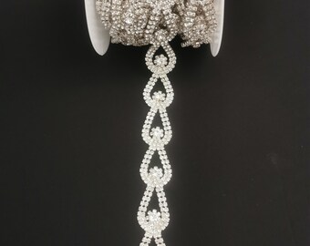 May include: A silver rhinestone trim with a teardrop design. The trim is on a spool and is ready to be used for embellishing clothing, accessories, or home decor.