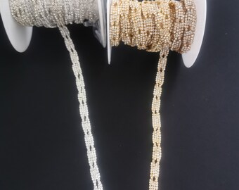 May include: Two spools of rhinestone trim, one silver and one gold. The trim is made of small, square rhinestones.