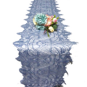 Könnte beinhalten: Blauer Tischläufer aus Spitze mit aufwendigem floralem Design. Ein Bouquet aus türkis, rosa und cremefarbenen Blumen schmückt den Läufer. Die Ränder des Läufers sind mit einem Wellenmuster versehen.