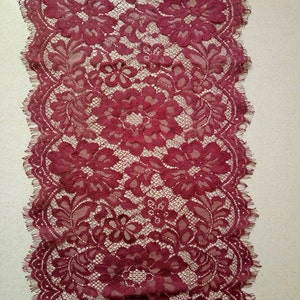May include: Burgundy lace trim with a floral pattern. The lace has a scalloped edge.