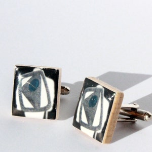 May include: A pair of silver cufflinks with black and white square ceramic inlays featuring a blue and white abstract design.
