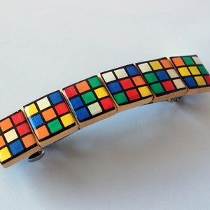 May include: A wooden hair clip with a row of colorful squares, resembling a Rubik's Cube, on top.