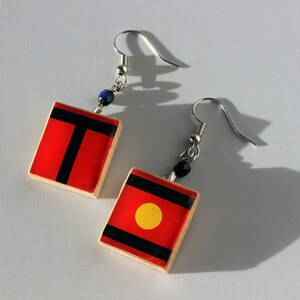 May include: A pair of earrings with red and black square-shaped pendants. One pendant has a black stripe and the other has a black stripe and a yellow circle.