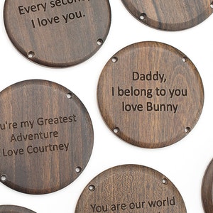 May include: A collection of dark brown wooden coasters with engraved messages. The messages include phrases like "Every second, I love you," and "You are our world." Each coaster has small holes around the edge.