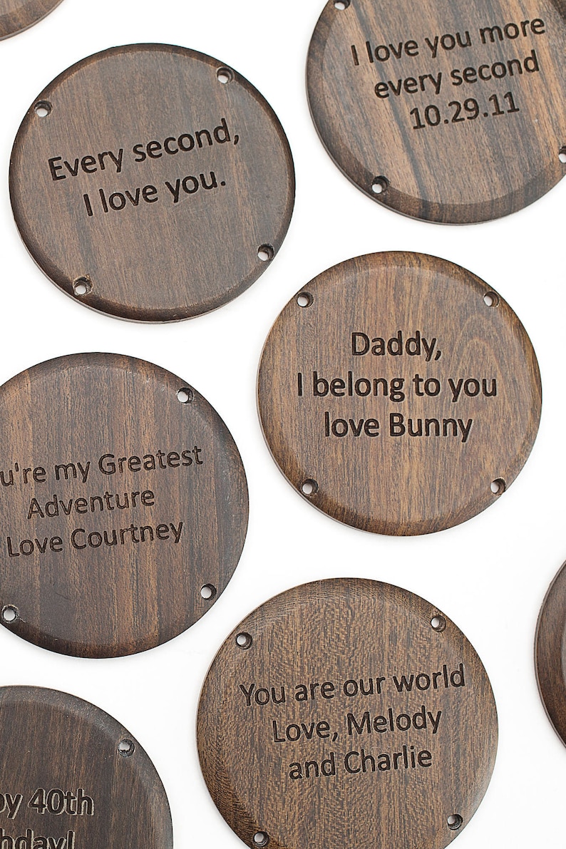 May include: A collection of dark brown wooden coasters with engraved messages. The messages include phrases like "Every second, I love you," and "You are our world." Each coaster has small holes around the edge.