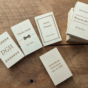 May include: Five wooden boxes with engraved text. The boxes are labelled with names and titles such as "Best Man", "Groomsman", and "DGH".