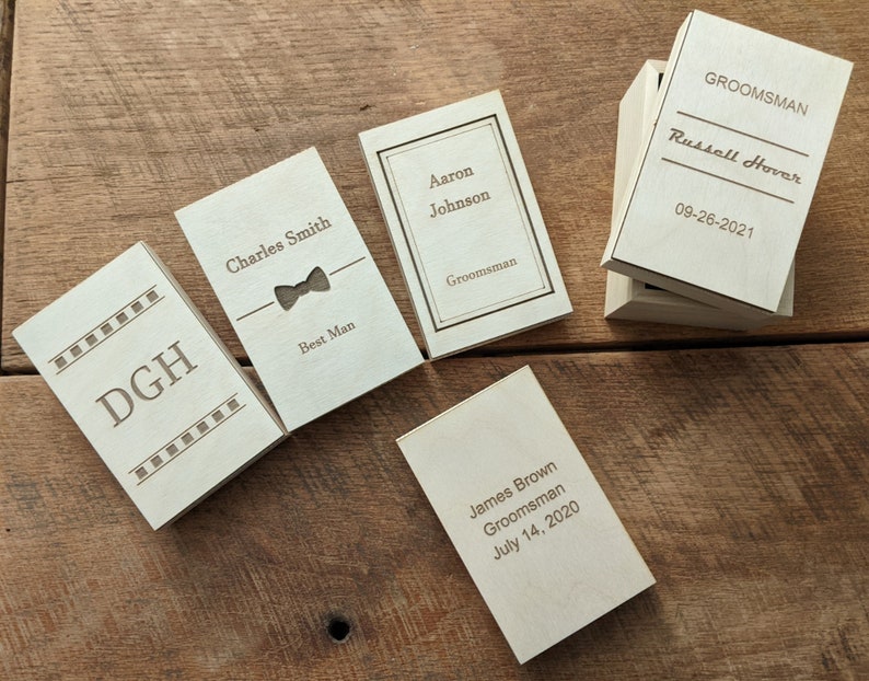 May include: Five wooden boxes with engraved text. The boxes are labelled with names and titles such as "Best Man", "Groomsman", and "DGH".