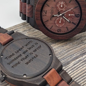 Men's wood watch in dark reddish color siting on a wood veneered ground with engraved text on the back site "Time spent with  someone you love is time that is never wasted"