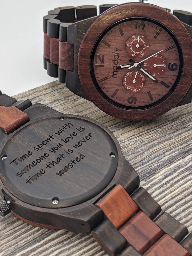 Men's wood watch in dark reddish color siting on a wood veneered ground with engraved text on the back site "Time spent with  someone you love is time that is never wasted"