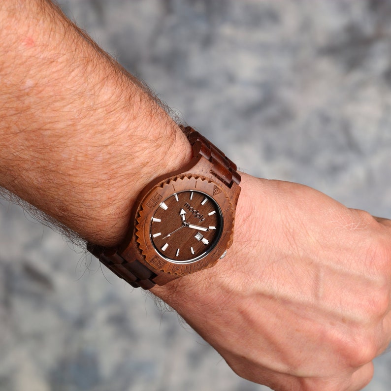 May include: A brown wooden wristwatch with a black face and white markings. The watch has a unique design with a wooden band and a circular face.