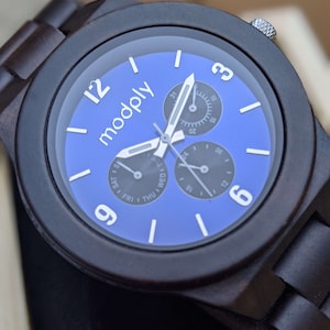 Op de afbeelding: Een donkerbruin houten polshorloge met een blauwe wijzerplaat. Het horloge heeft drie subwijzerplaten en het woord "modply" staat op de wijzerplaat gedrukt.