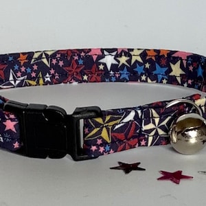 May include: A blue cat collar with a colourful star pattern and a silver bell. The collar is adjustable and has a safety release buckle.