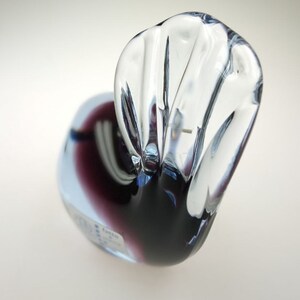 May include: A clear glass sculpture of a bird with a purple and blue iridescent finish. The bird's head is tilted back and its wings are spread out.