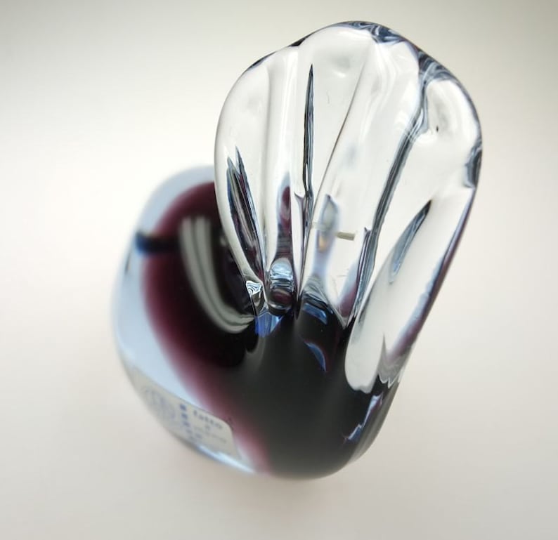 May include: A clear glass sculpture of a bird with a purple and blue iridescent finish. The bird's head is tilted back and its wings are spread out.
