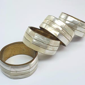 Puede incluir: Juego de cuatro anillos de servilleta blancos y dorados con un patrón geométrico. Los anillos están hechos de latón y madreperla.