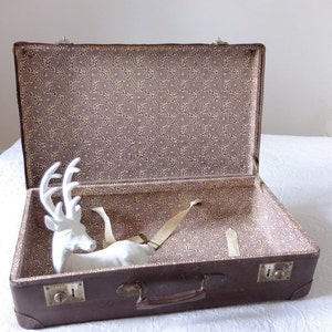 May include: An open brown vintage suitcase with a white porcelain deer figurine inside. The suitcase has a floral patterned lining and a brown leather handle.