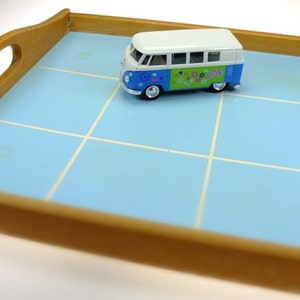 Puede incluir: Un autob&uacute;s Volkswagen de juguete azul y blanco con un s&iacute;mbolo de paz y la palabra "love" en el lateral, sentado en una bandeja de azulejos azul y blanco.