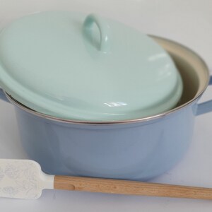 Könnte beinhalten: Ein hellblauer Emailletopf mit passendem hellblauem Deckel und einem Holzspatel mit weißem Blumenmuster.