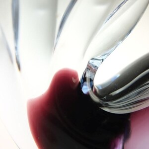 May include: Close-up of a glass vase with a swirling, abstract design. The vase is clear with a dark purple and black color at the bottom.