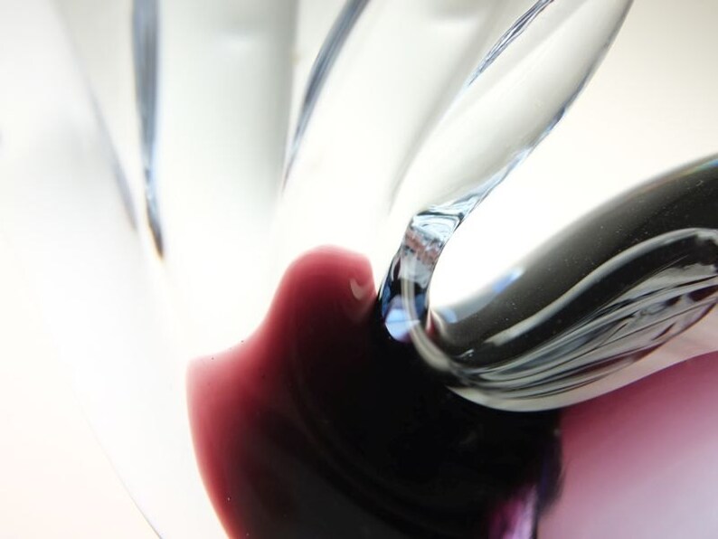 May include: Close-up of a glass vase with a swirling, abstract design. The vase is clear with a dark purple and black color at the bottom.