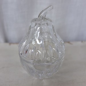 Könnte beinhalten: Ein durchsichtiger Glasbehälter in Birnenform mit Deckel. Der Behälter hat ein dekoratives, facettiertes Design.