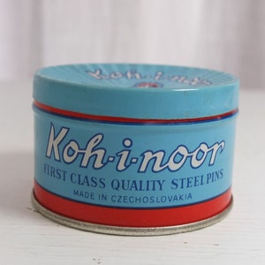 Puede incluir: Una lata redonda y vintage con cuerpo azul claro, base roja y ribetes rojos y azules. La lata dice "Koh-i-noor FIRST CLASS QUALITY STEEL PINS MADE IN CZECHOSLOVAKIA" en letras blancas.