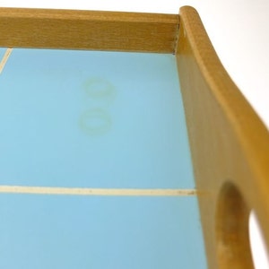 Puede incluir: Una bandeja de servir de madera con una parte superior de azulejos de color azul claro. Los azulejos tienen un mortero blanco y hay dos marcas de agua marrones tenues en la superficie.