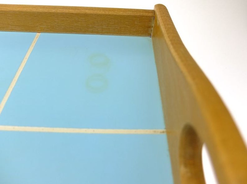 Puede incluir: Una bandeja de servir de madera con una parte superior de azulejos de color azul claro. Los azulejos tienen un mortero blanco y hay dos marcas de agua marrones tenues en la superficie.