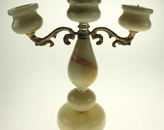 May include: A three-armed candelabra with a cream-colored onyx base and candle cups. The arms are gold-colored metal with a decorative design. The candelabra is designed to hold three candles.