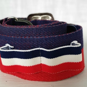 Op de afbeelding: Een blauwe, witte en rode gestreepte stoffen riem met een zilveren gesp.