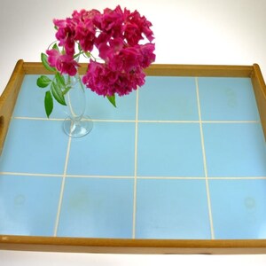 Puede incluir: Una bandeja de servir de madera con una superficie de azulejos de color azul claro. La bandeja tiene dos asas a los lados y est&aacute; decorada con un jarr&oacute;n de flores rosas.
