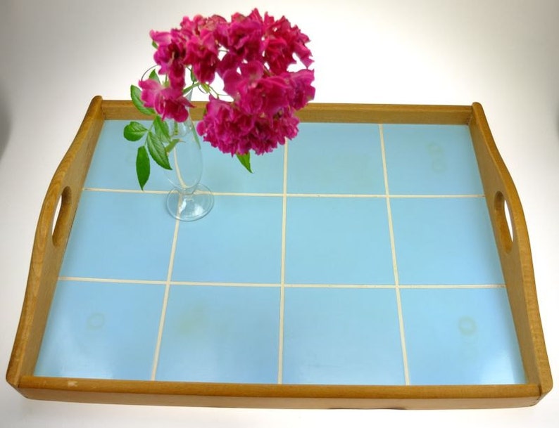 Puede incluir: Una bandeja de servir de madera con una superficie de azulejos de color azul claro. La bandeja tiene dos asas a los lados y est&aacute; decorada con un jarr&oacute;n de flores rosas.