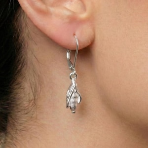May include: Silver-toned dangle earrings. Each earring features a detailed, stylized corn design with a small, round bead at the bottom. The earrings are attached to a lever-back closure. The image shows the earring worn on a person's ear.