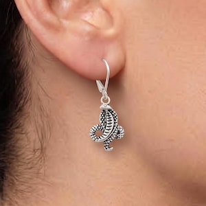May include: A silver-toned earring featuring a detailed cobra snake pendant with a textured, oxidised finish. The snake is depicted in a coiled position, hanging from a simple silver wire hook that passes through the earlobe for secure placement.