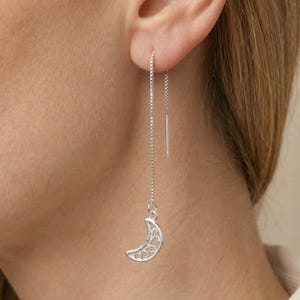Pode incluir: Brincos de fio de prata com um pingente de lua crescente. O pingente de lua tem um design delicado e vazado. Estes brincos pendurados são leves, adicionando um toque de elegância celestial a qualquer look.