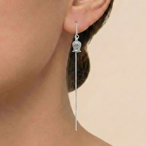 Puede incluir: Un pendiente colgante de color plateado con un diseño en forma de tulipán. El pendiente cuelga de una fina cadena, creando un aspecto delicado y elegante. El pendiente se lleva en la oreja.