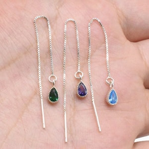 Może przedstawiać: Trzy pary srebrnych kolczyków wiszących z kamieniami szlachetnymi w kształcie łzy. Kolczyki mają zielony, fioletowy i niebieski kamień szlachetny.