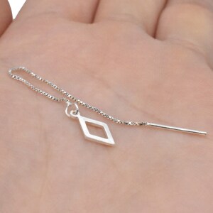 Puede incluir: Una cadena de plata con un colgante en forma de diamante y una fina varilla de plata. La cadena es delicada y el colgante es sencillo.