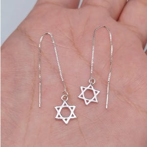 Puede incluir: Un par de pendientes de plata con un colgante de estrella de David en cada pendiente.